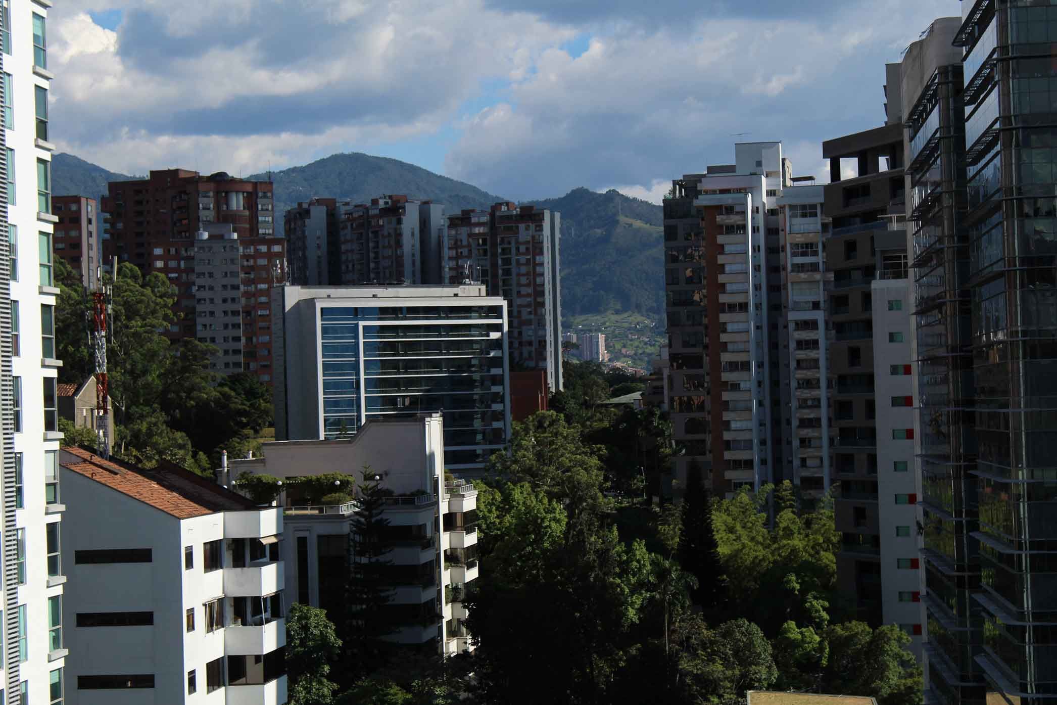 A dense city skyline with numerous high-rise buildings and distant mountains under a cloudy sky.