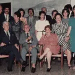 A group of twelve men and women pose for a formal photograph in what appears to be an indoor setting.