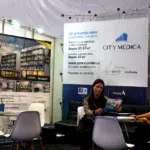 Woman at a booth with a City Medica banner behind her.