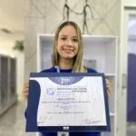 A smiling young woman holds a certificate with a blue folder.