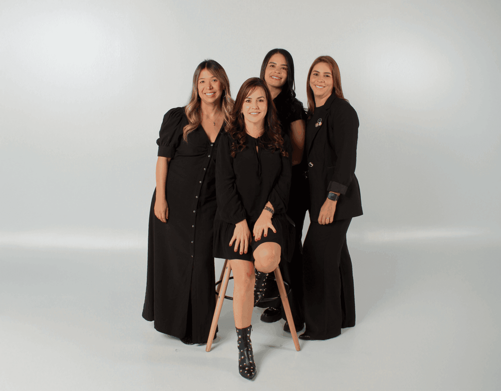 Four women in black professional attire pose for a studio photograph against a white background.
