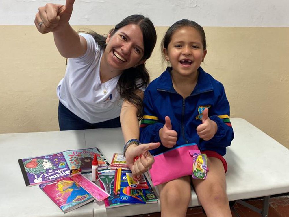 A smiling woman and a young girl give thumbs up beside school supplies.