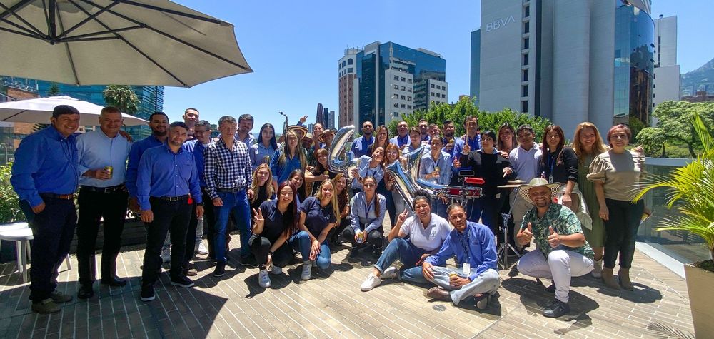 A large group of people pose for a photo on a wooden deck with buildings in the background.