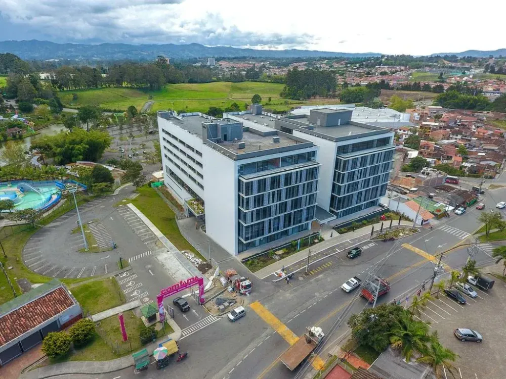 Modern multi-story office building with reflective windows and white facade, surrounded by greenery and a road.