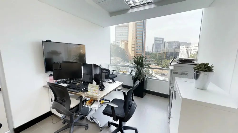 Modern office space with multiple computer monitors, ergonomic chairs, and a large window overlooking a city skyline.