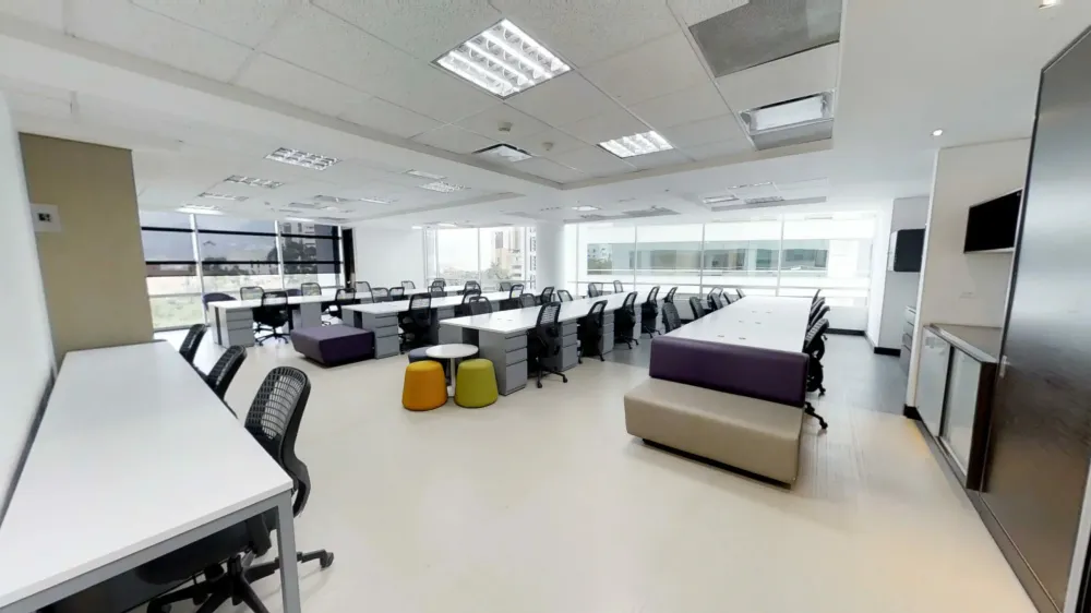 Modern office space with individual desks, collaborative seating areas, and large windows.