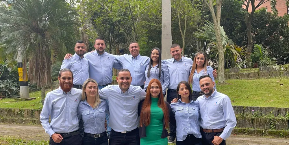 Eleven smiling professionals, a diverse team, pose outdoors in light blue shirts.