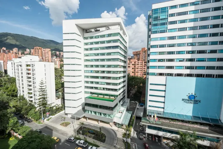 Modern white and glass office buildings stand tall against a blue sky with green hills in the background.